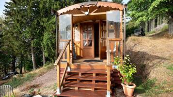 A wooden cabin with a wooden staircase leading to a door, surrounded by trees.
