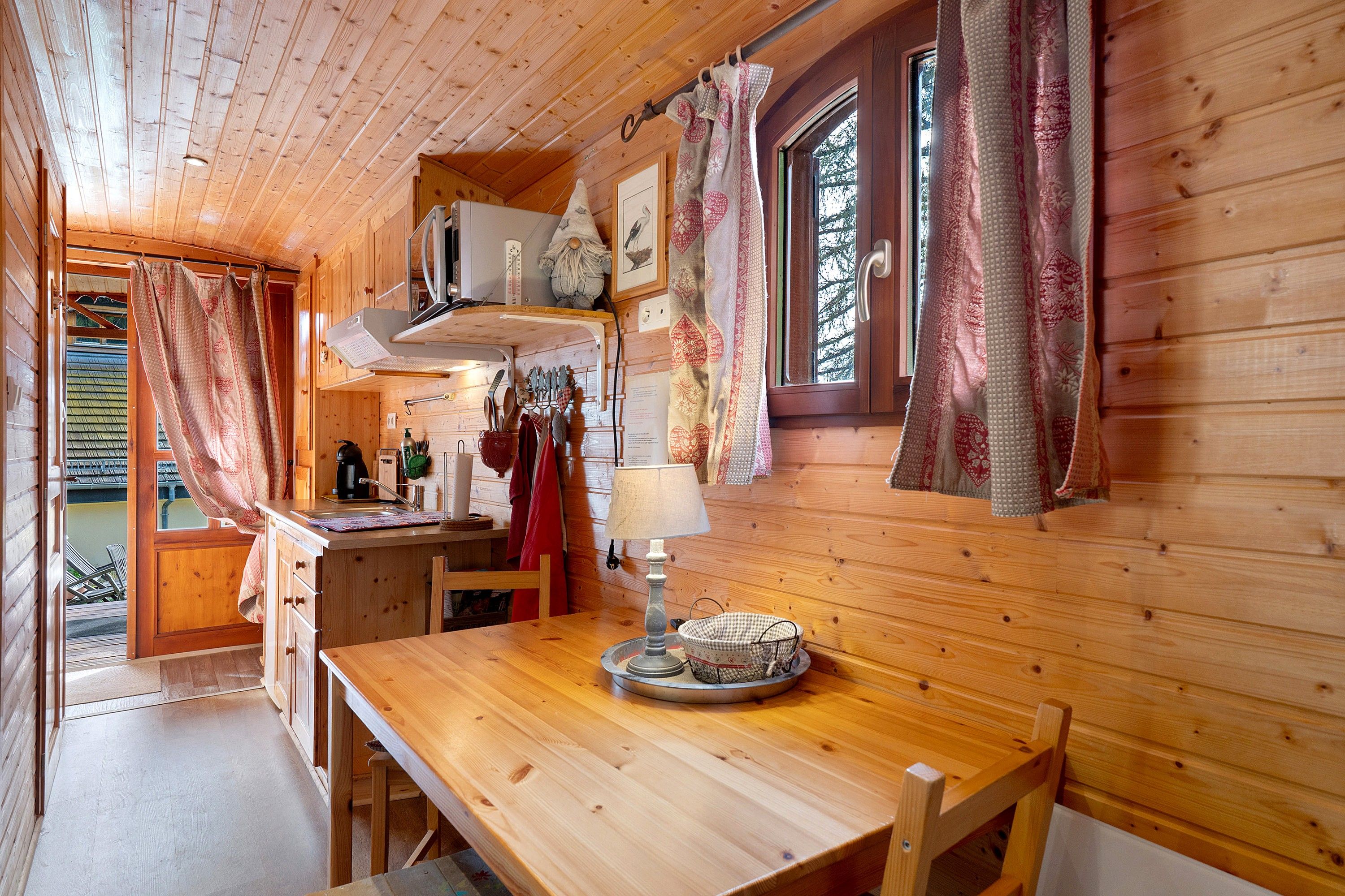 A wooden interior with a kitchen area, including a table, chairs, and a window with curtains.