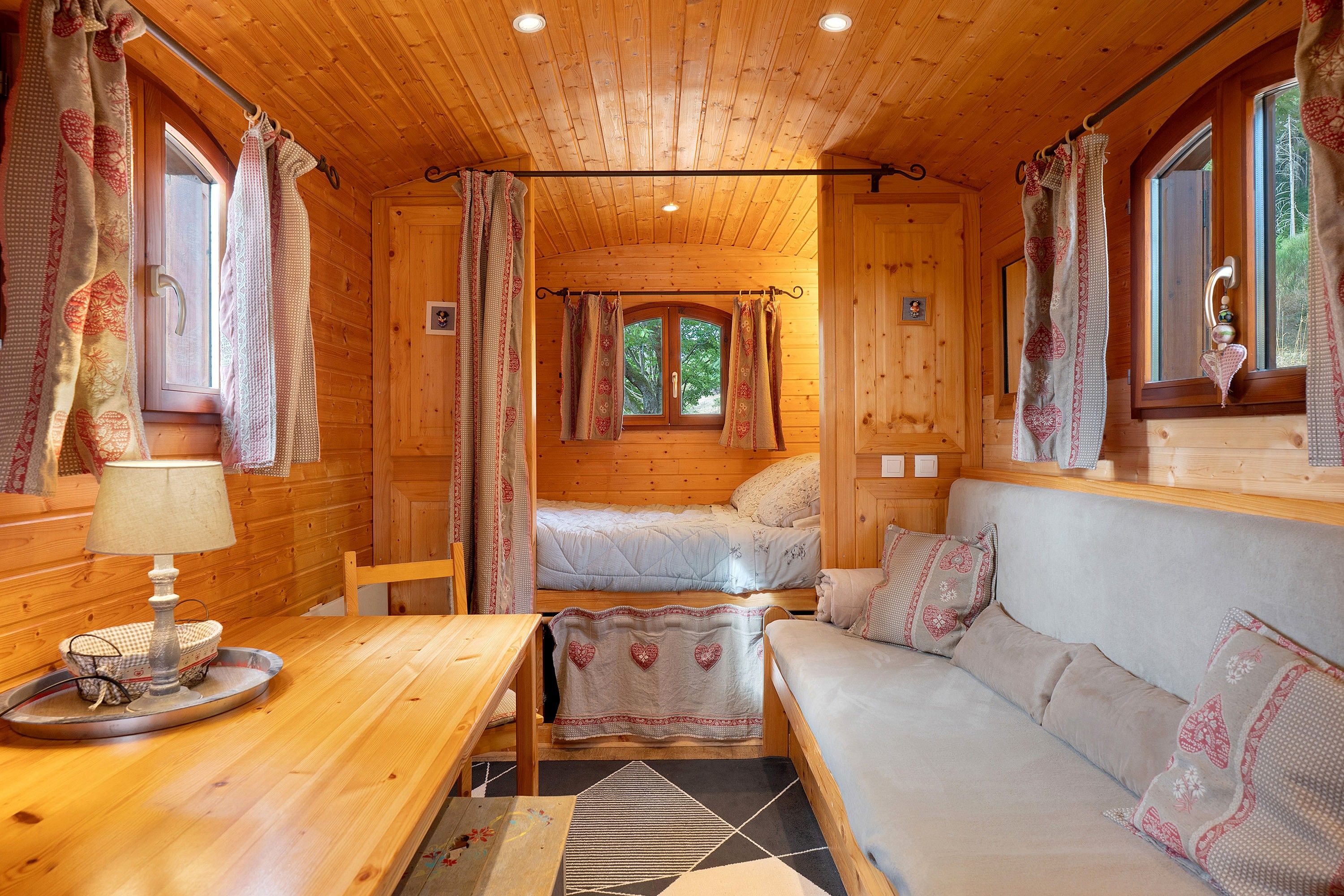 Ein gemütliches Blockhaus-Interieur mit Holzausstattung, einer Couch, einem Tisch und einem Fenster mit Vorhängen.
