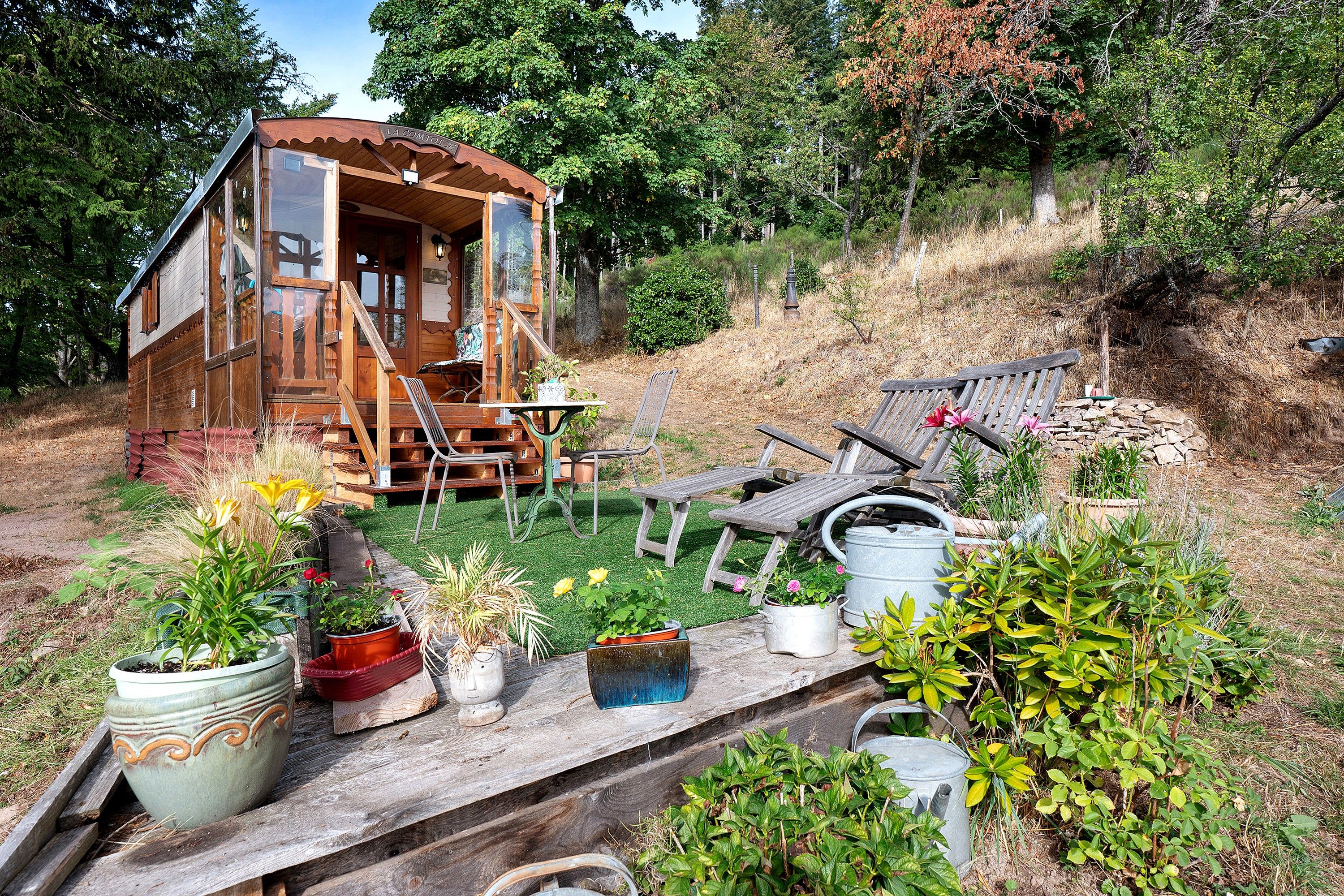 A rustic wooden cabin with a porch and a small garden area with potted plants and outdoor furniture.