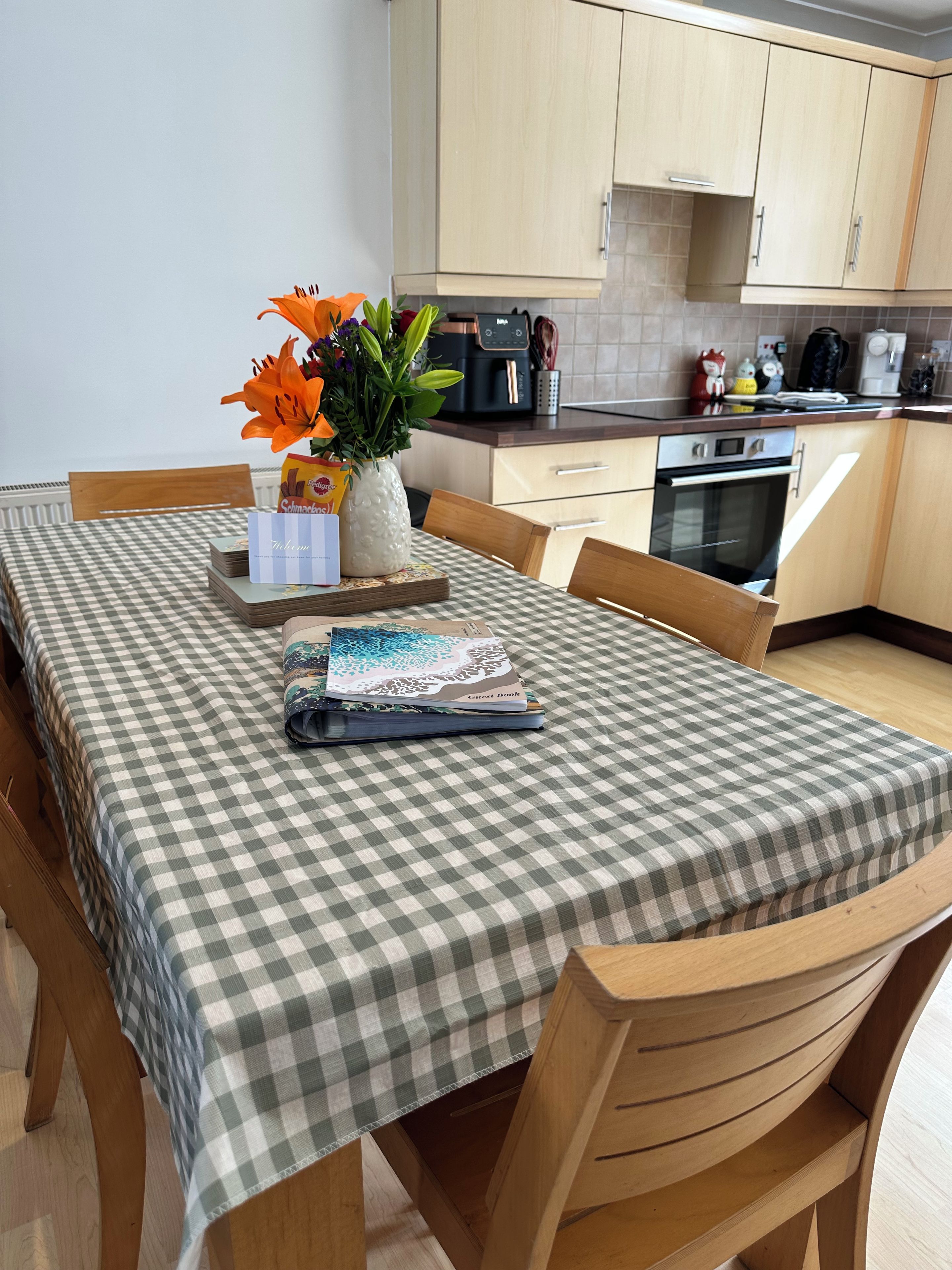 A dining table with a checkered tablecloth, a vase with flowers, a guest book, and a stack of books.