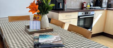 Una mesa de comedor con mantel a cuadros, un jarrón con flores, un libro de visitas y una pila de libros.