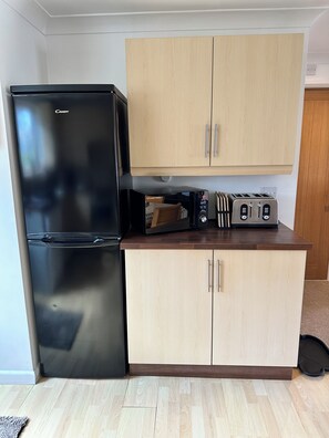 Eine kompakte Küche mit einem schwarzen Kühlschrank, einer Mikrowelle, einem Toaster und Holzschränken.