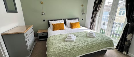 Un dormitorio con cama, mesita de noche, cómoda y ventana con cortinas.