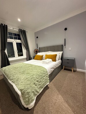 Ein Schlafzimmer mit einem Bett, einem Nachttisch, einem Fenster mit Vorhängen und einem Wandventilator.