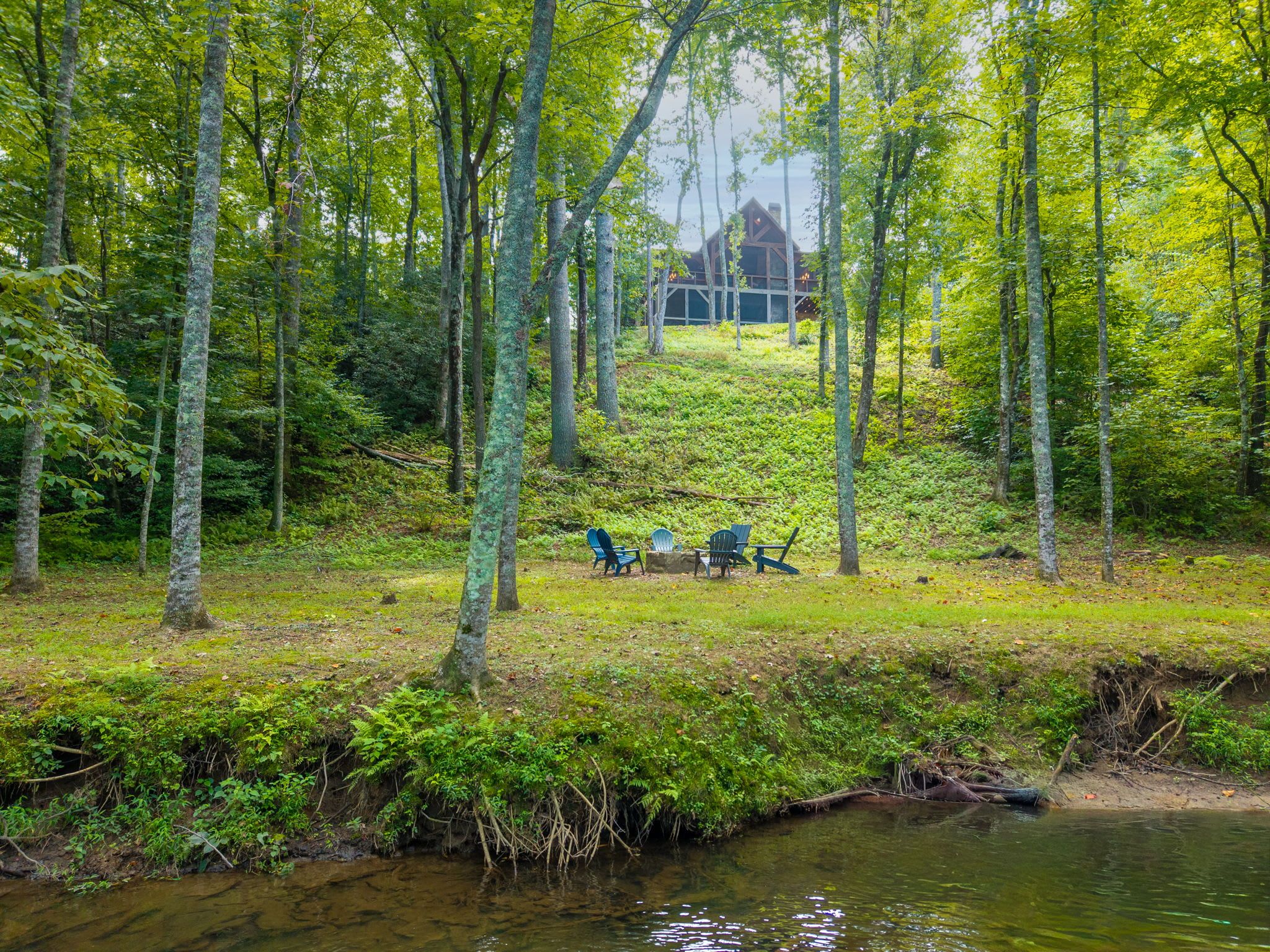 A forested area with a small clearing, a body of water, and a building in the background.