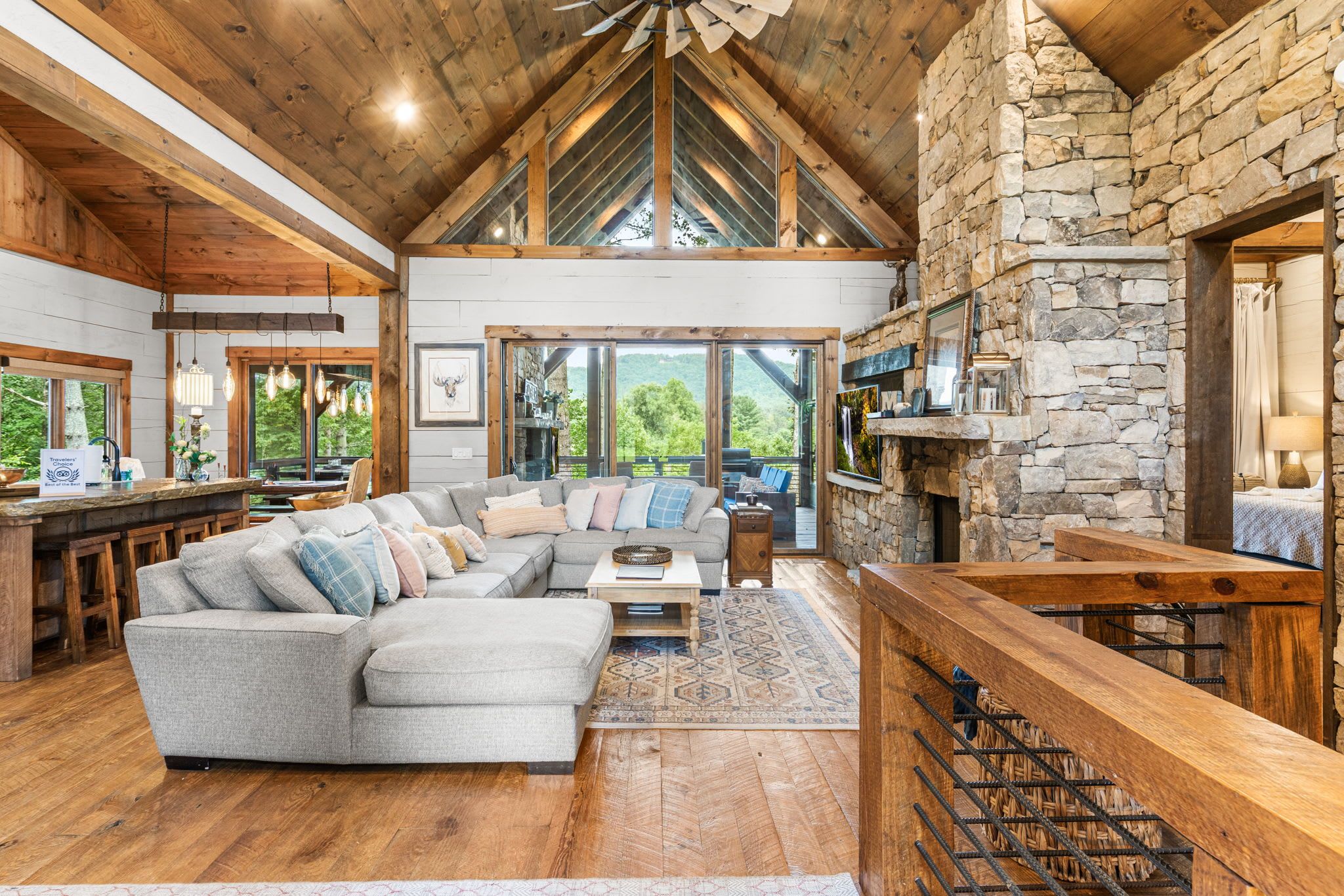 A spacious living area with a large sectional sofa, a stone fireplace, and a wooden ceiling.