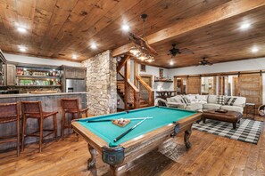 A pool table in a wooden-floored room with a stone wall, bar area, and a sofa. - Hot Tub, Mountain Views, Games & Outdoor Living (Epworth)