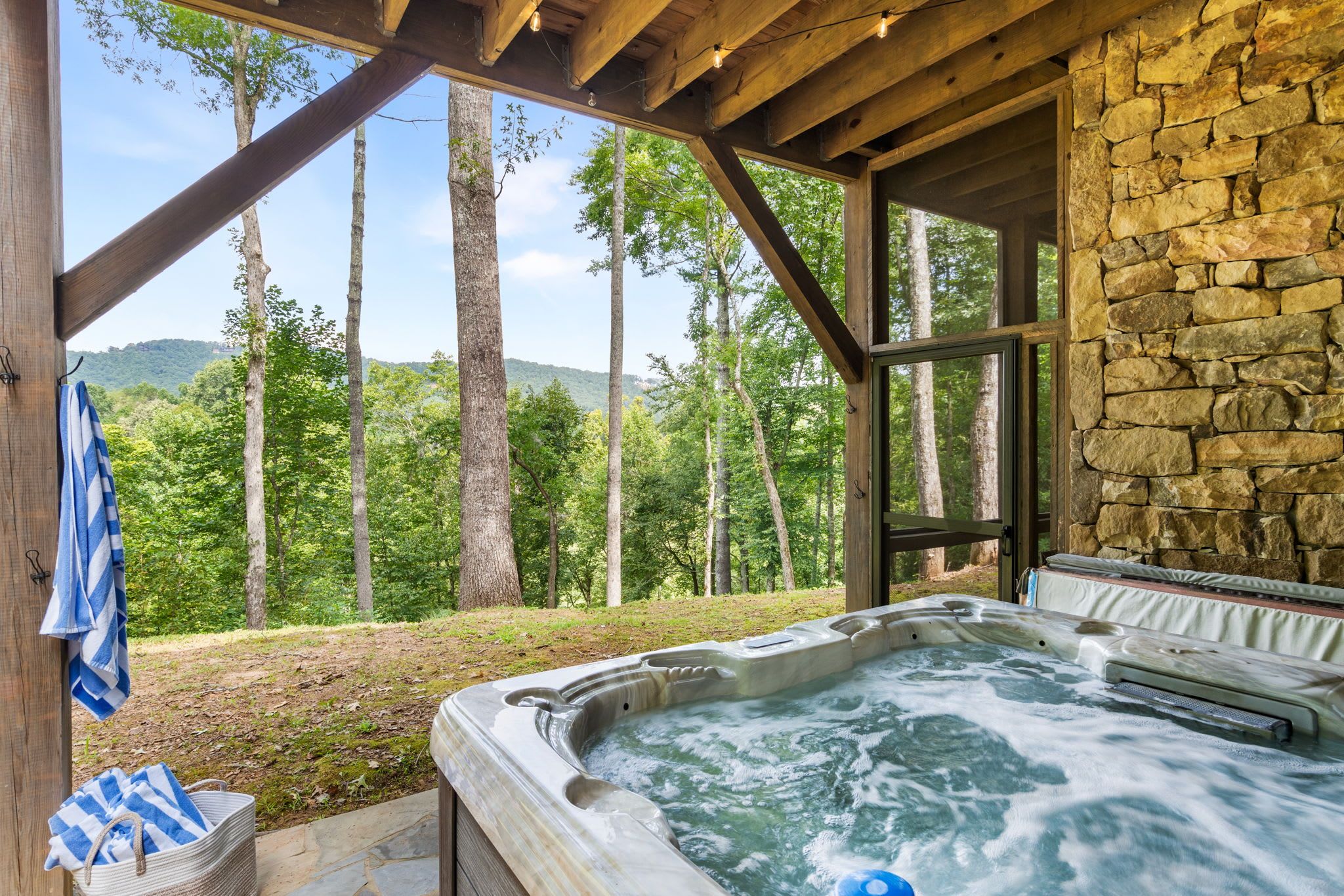 Ein Whirlpool in einer Holzhütte mit Steinwand und Blick auf einen Wald.