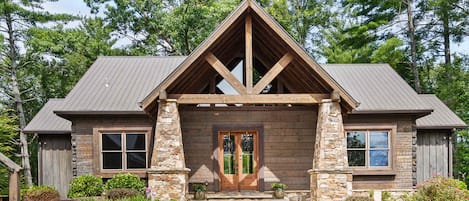 A log cabin with a stone chimney, a front porch, and a metal roof.