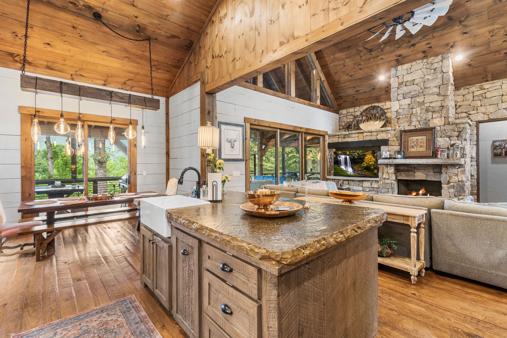 A spacious kitchen with a stone fireplace, wooden cabinets, and a large island with a copper bowl.