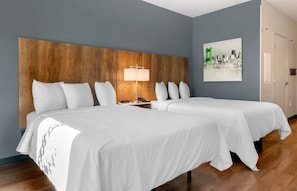 Ein Hotelzimmer mit zwei Betten, einem hölzernen Kopfteil, einem Nachttisch mit Lampe und einem Stadtbild an der Wand.