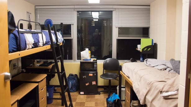 Un dormitorio con literas, un escritorio, una silla, un microondas y una ventana.