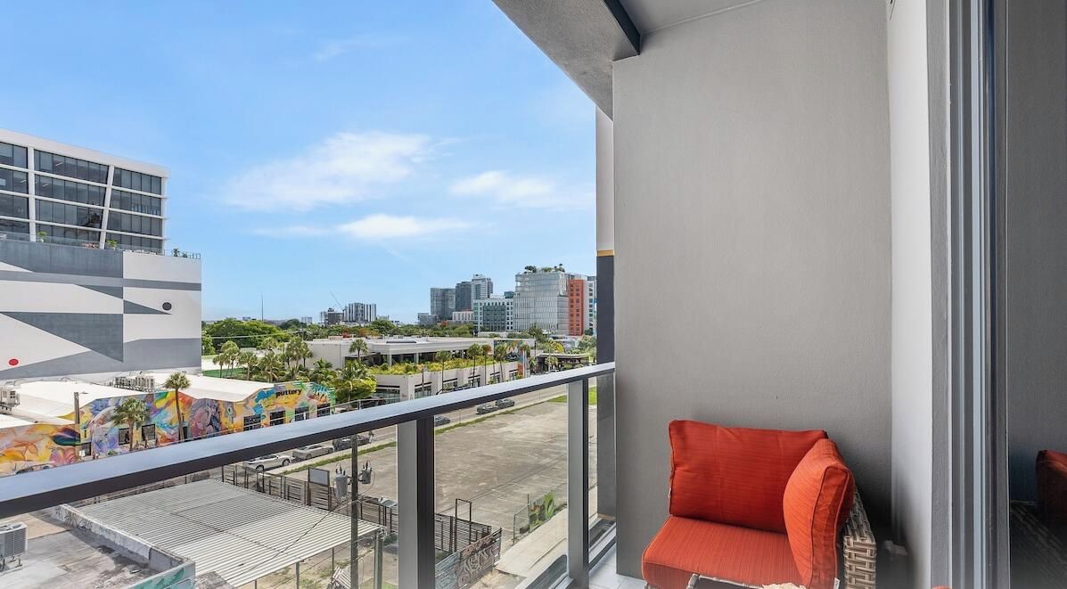 Un balcón con vistas a un paisaje urbano, una silla roja y un edificio moderno con ventanas de vidrio.