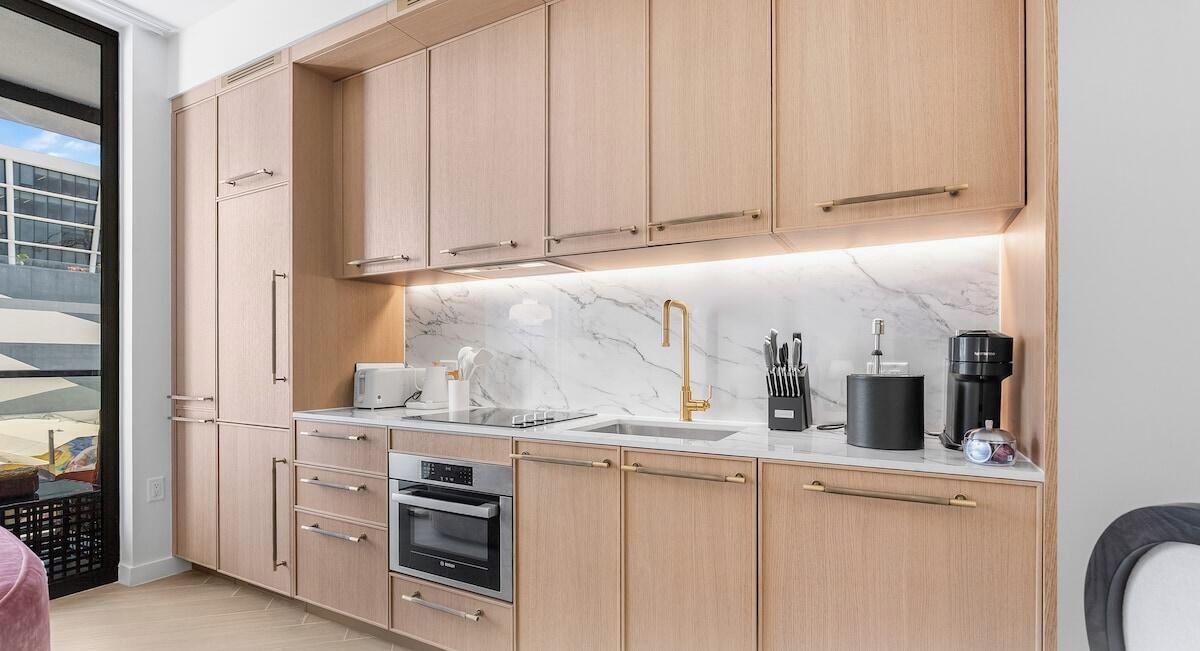 Una cocina moderna con armarios de madera, horno empotrado, lavaplatos y cafetera.