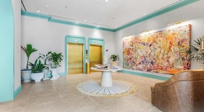A lobby with a round table, two elevators, and a large abstract painting. - Studio w/ Pool & Bar in NoMad Residences Wynwood (Miami)