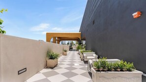 Eine Dachterrasse mit Schachbrettmuster-Boden, Kübelpflanzen, Außenmöbeln und Blick auf die Stadtlandschaft.