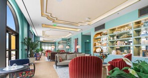 Un hall d’hôtel doté d’un espace salon, d’une bibliothèque et d’une grande fenêtre.