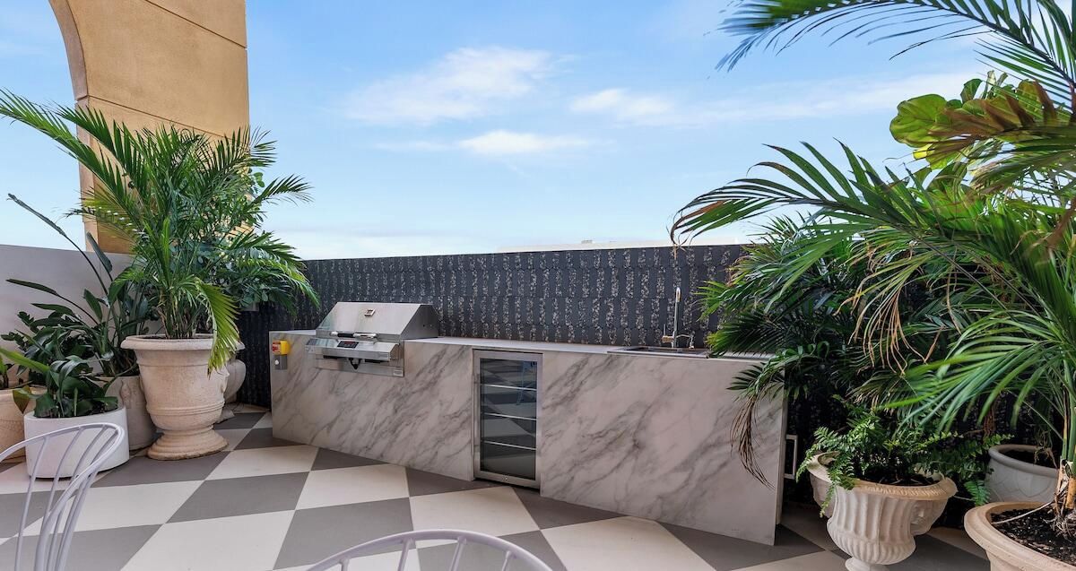 Un área de patio exterior con piso de baldosas de mármol, una estación de parrilla integrada y plantas en macetas.