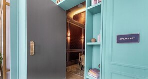 Un couloir avec une porte fermée, une bibliothèque remplie de livres et une pancarte indiquant « SPEAKEASY ».