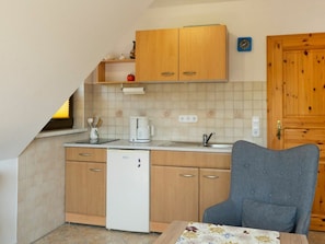 Eine kleine Küche mit Holzschränken, einem weißen Kühlschrank, einer Kaffeemaschine und einem Spülbecken.