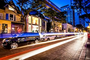 Una strada di notte con edifici moderni, un marciapiede alberato e auto parcheggiate.
