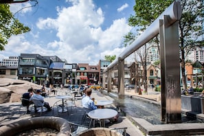 Una piazza pubblica con posti a sedere all'aperto, una fontana e edifici moderni sullo sfondo.