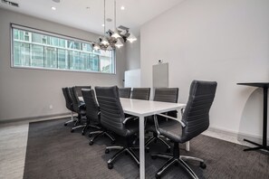 A conference room with a long table, six black office chairs, a whiteboard, and a modern chandelier.