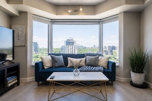 A modern living room with a blue sofa, a coffee table, and a city view through large windows.