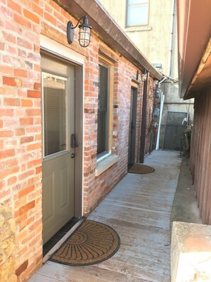 Un étroit sentier pavé de briques mène à une porte dotée d’une fenêtre et d’une sonnette.