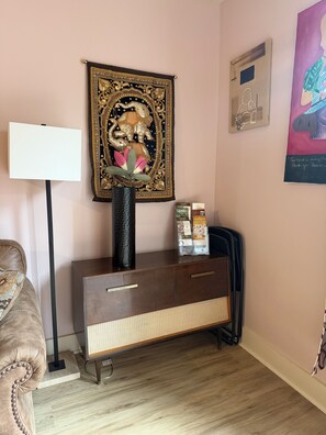 Une pièce comprenant un meuble en bois de style ancien, une tapisserie décorative ornée d’un motif d’éléphant, un lampadaire et une œuvre d’art encadrée accrochée au mur.