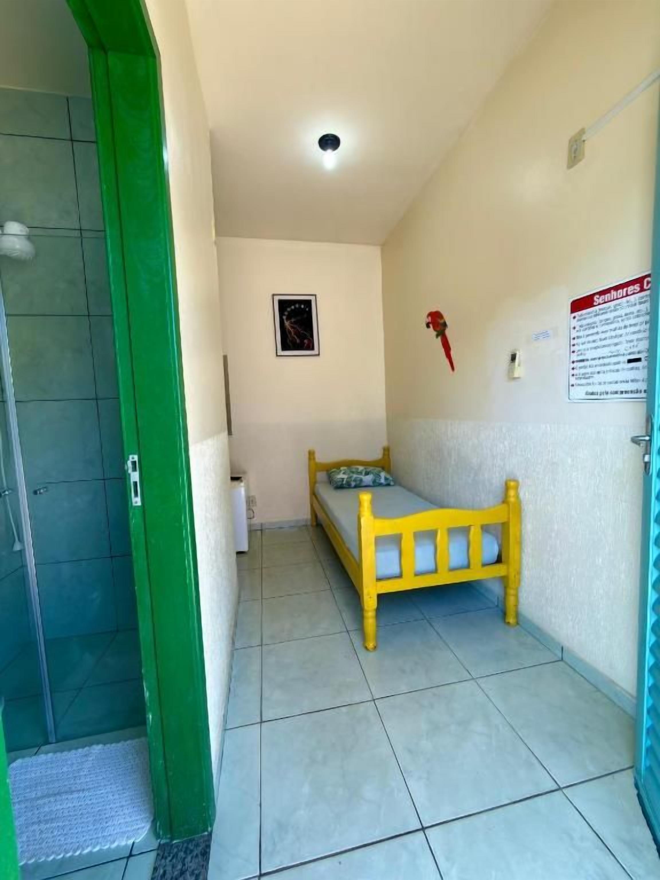 Una habitación pequeña con una cama, una puerta verde y piso de baldosas.