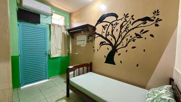 Una habitación con una cama, un mural en la pared, una puerta verde y una ventana con cortina.