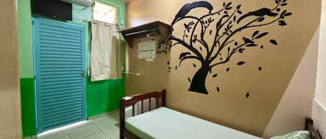 A room with a bed, a wall mural, a green door, and a window with a curtain.