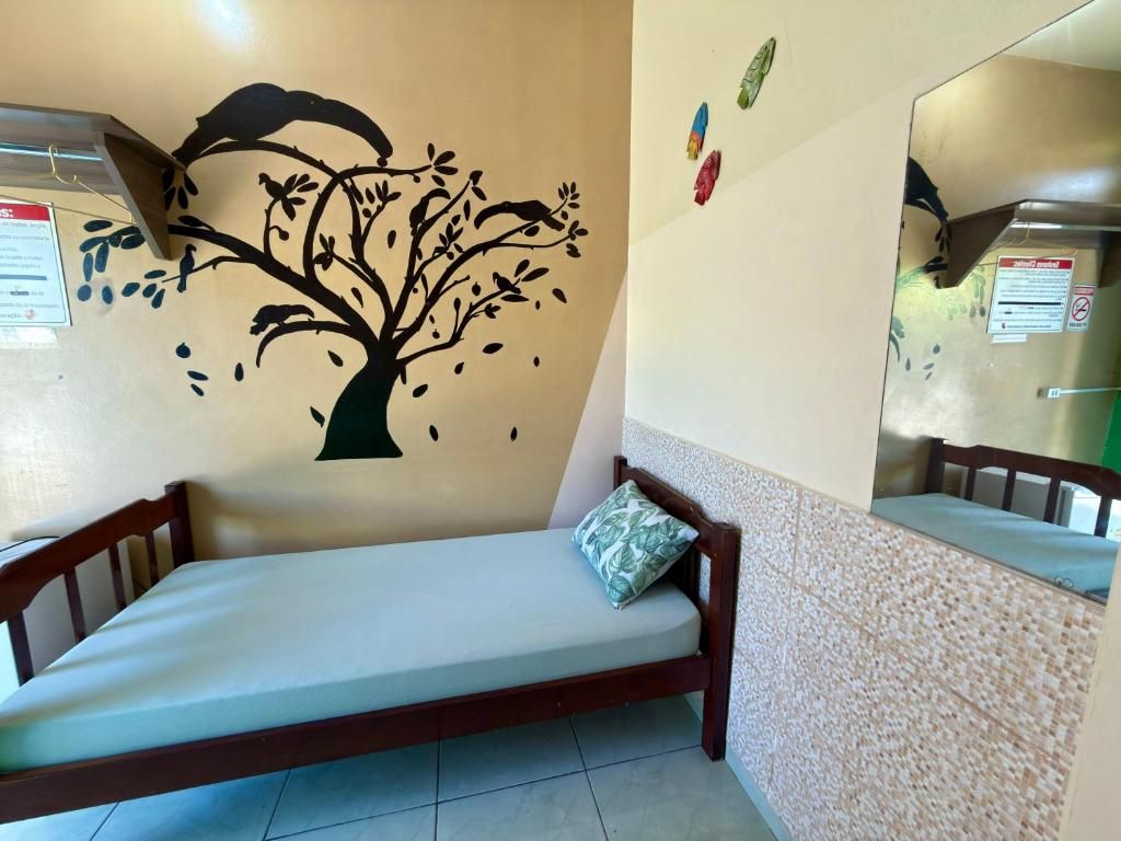 Una cama individual con estructura de madera y colchón blanco, una pared con un adhesivo de árbol y un piso de baldosas.