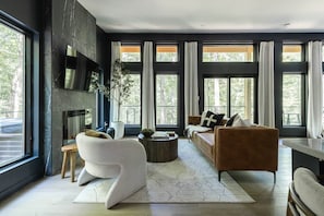 A modern living room with a fireplace, large windows, and a sofa. - The Den at Dunlap Ridge (Laurel Township)
