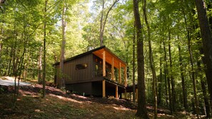 A cabin in a forest with a wooden deck and large windows. - The Den at Dunlap Ridge (Laurel Township)