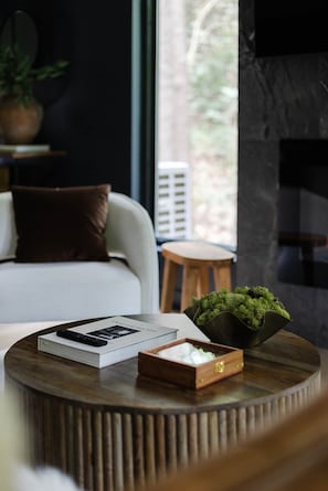 A modern living room with a sofa, a round wooden coffee table, a small stool, and a potted plant. - The Den at Dunlap Ridge (Laurel Township)
