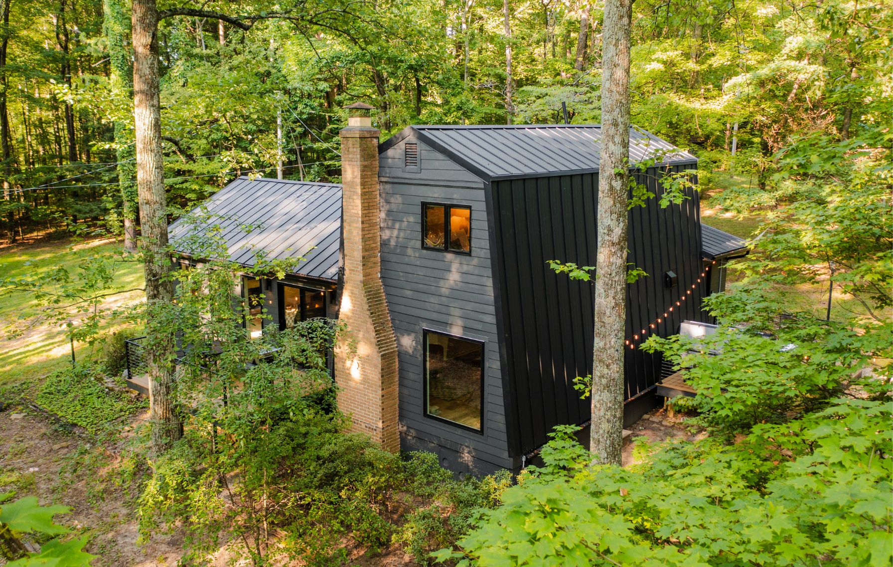 Eine moderne Hütte mit geneigtem Dach, großen Fenstern und Schornstein, umgeben von dichtem Wald.