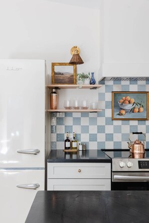 A modern kitchen with white cabinetry, a black countertop, and a checkered backsplash. - The Pine at Dunlap Ridge (Laurel Township)