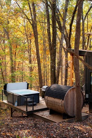 Ein Sitzbereich im Freien mit Grill und einer großen Tonne, umgeben von Bäumen mit Herbstlaub.