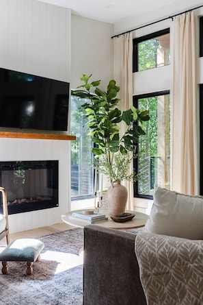 A modern living room with a fireplace, a large flat-screen TV, a potted plant, and a comfortable seating area. - The Pine at Dunlap Ridge (Laurel Township)