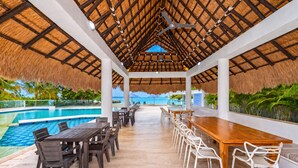 An indoor pool area with a thatched roof, wooden tables, and chairs, overlooking a clear blue pool. - CASA PRIVADA 5 - AREIA BARU (Bolívar)
