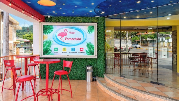 A hotel lobby with a large digital screen displaying amenities, red chairs, and a green wall. - HOTEL ESMERALDA EN POZA RICA VERACRUZ MX (POZA RICA)