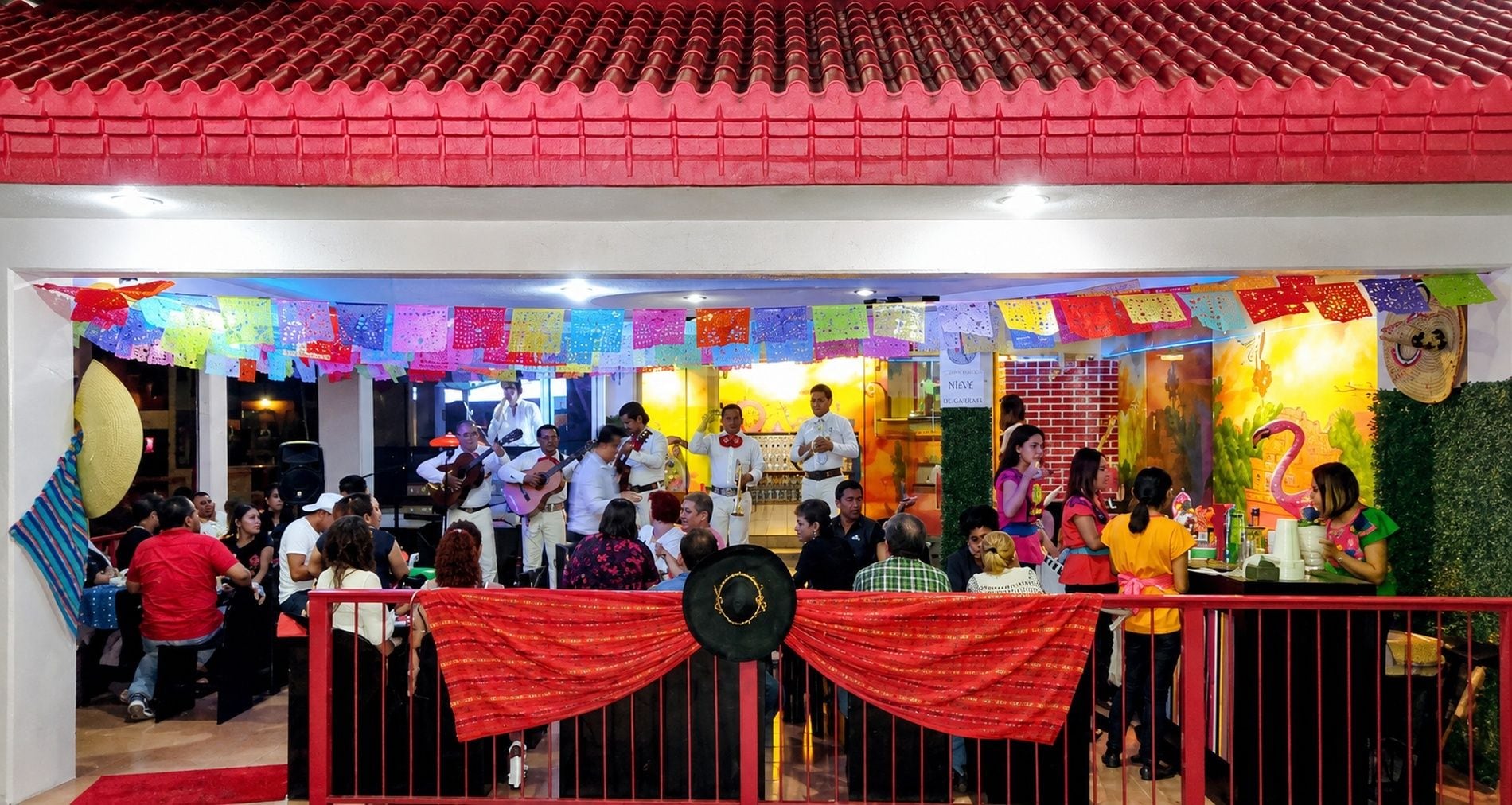 A restaurant with a red tiled roof, colorful decorations, and a group of people dining.