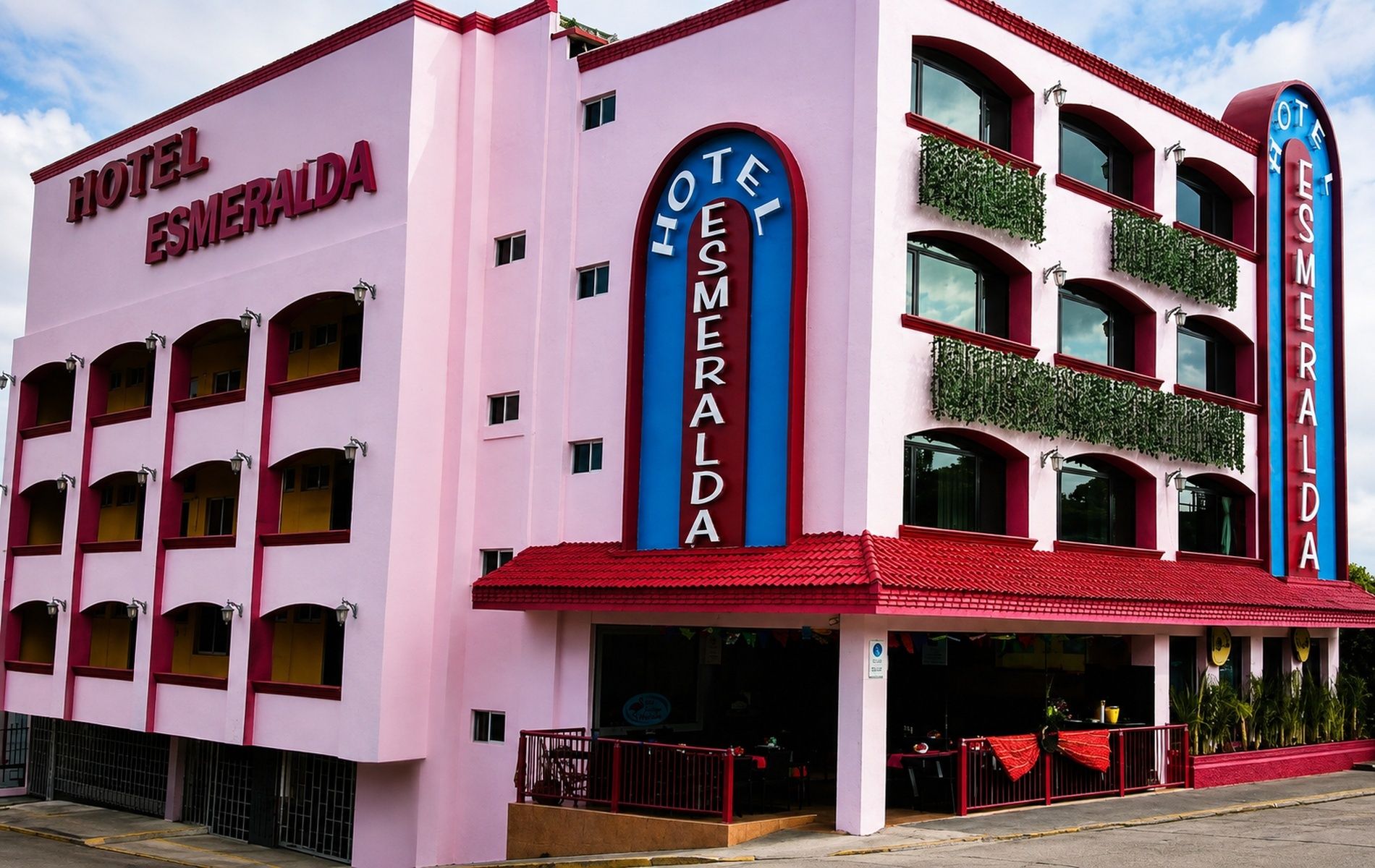 Een roze en rode hotelgevel met meerdere balkons en een bord waarop 'Hotel Esmeralda' staat.