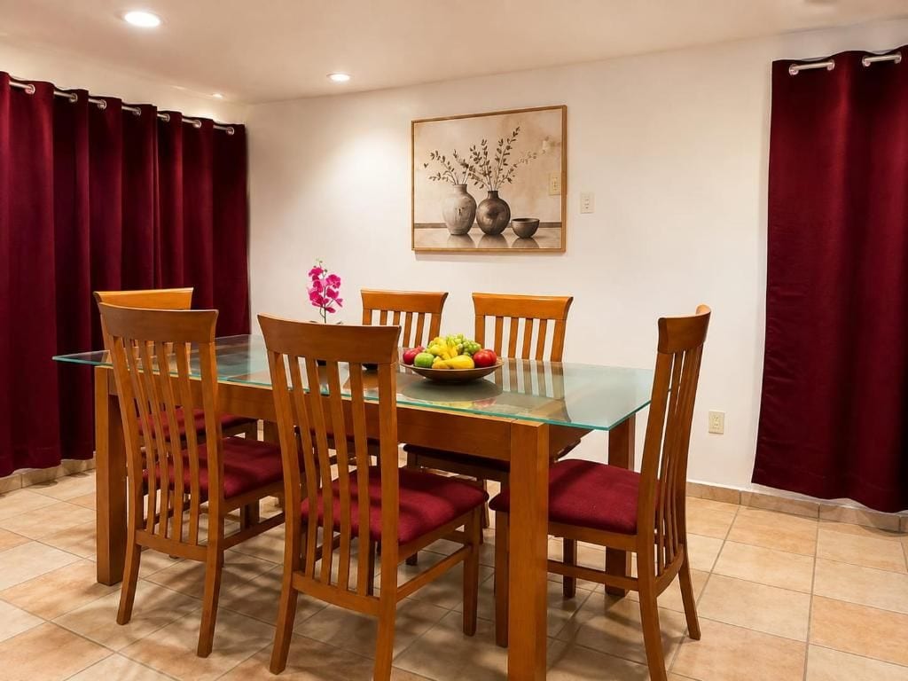 A dining area with a glass-top table, wooden chairs, and a fruit bowl.