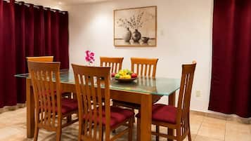 A dining area with a glass-top table, wooden chairs, and a fruit bowl.
