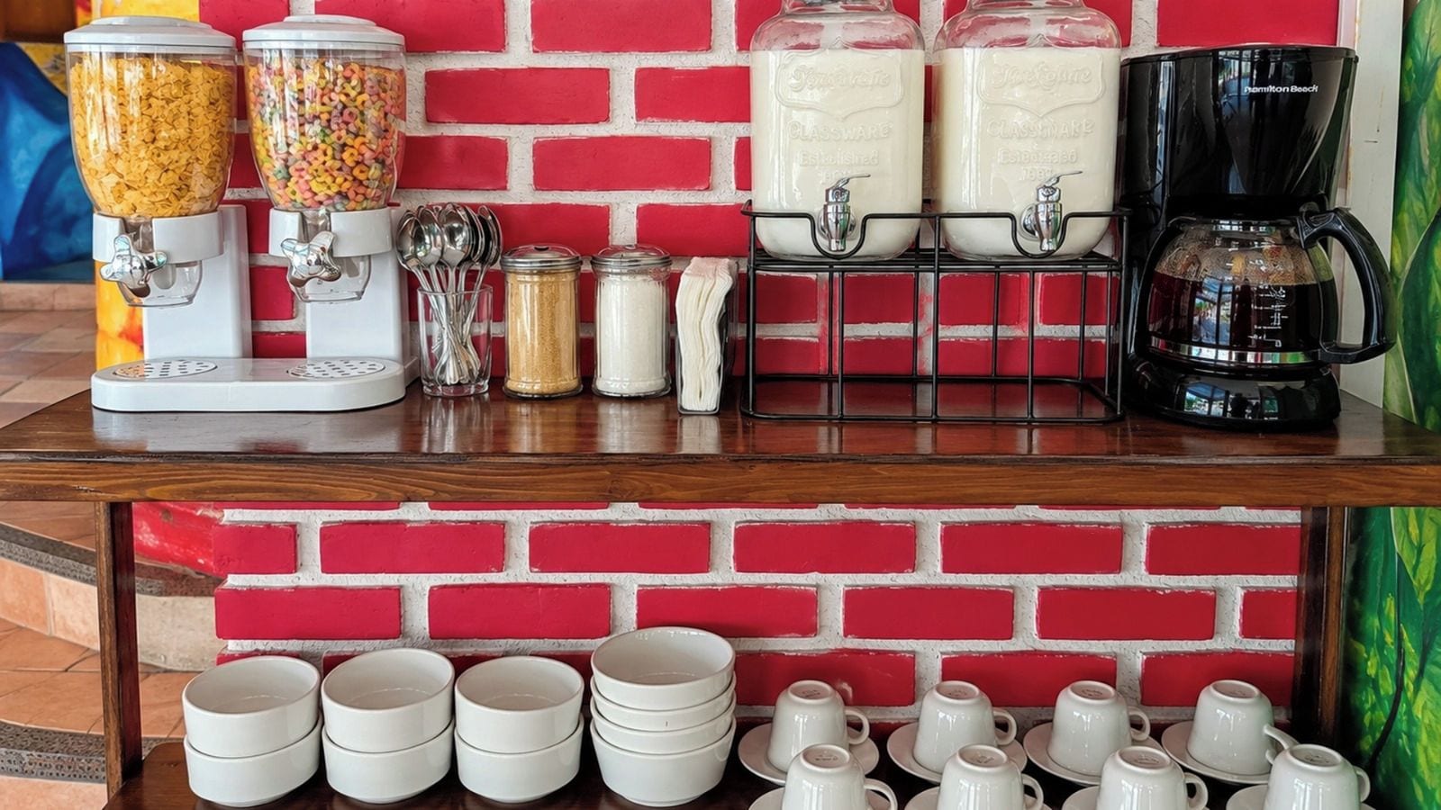 A breakfast bar with cereal dispensers, a coffee maker, and a brick-patterned wall.