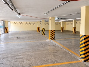 A parking garage with concrete floors, yellow and black striped pillars, and ventilation ducts on the ceiling.